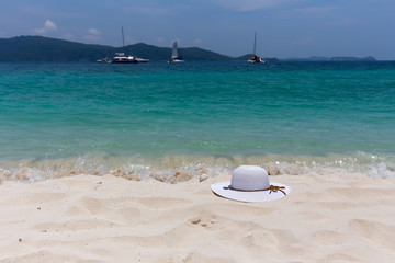 Fototapeta na wymiar A white female hat lies on the sand on the seashore. Beautiful view of the seascape with the ships on the horizon.
