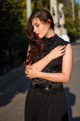 Young, beautiful girl in a black dress with a corset, on a park background and stone columns with lanterns.