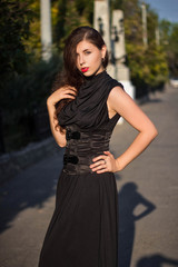 Young, beautiful girl in a black dress with a corset, on a park background and stone columns with lanterns.