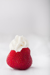 Obraz na płótnie Canvas Single strawberry with whipped cream on a white grey background. Vertical image. Copy space