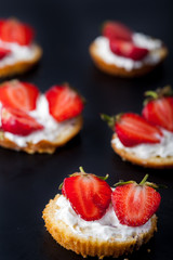 Fluffy buttermilk biscuits shortcake with red ripe strawberries and fresh whipped cream on a black background