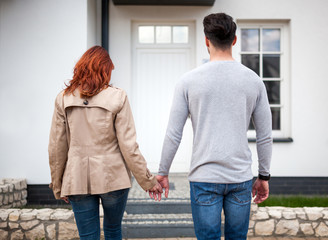 Happy couple in front of their new home against door, real estate concept