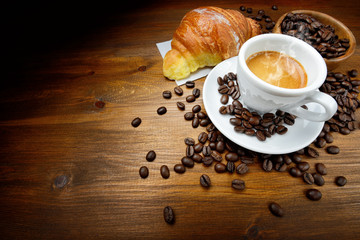 Espresso and croissant with coffee beans on wood background