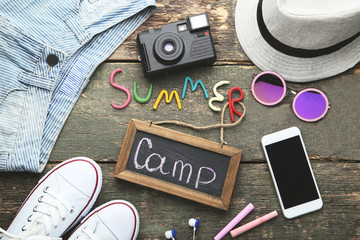 Inscription Summer Camp with smartphone, sunglasses and clothes on wooden table