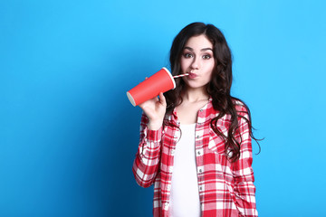 Young beautiful woman with paper cup on blue background