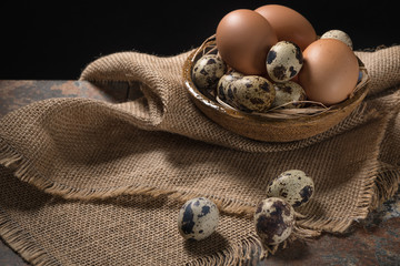 Chicken and quail eggs in bowl on rustic wooden background