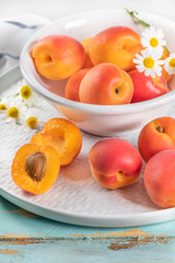 Naklejka na ściany i meble Delicious ripe apricots in a bowl on the wooden table. Close-up with apricots and daisy flowers