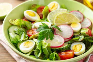 Fresh salad with vegetables and quail eggs on rustic wooden background