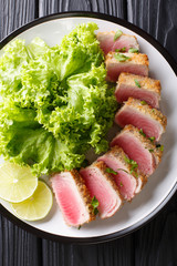 Delicious steak ahi tuna  in bread crumbs panko with lettuce and lime closeup on a black table....