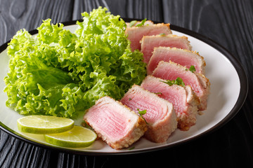 Healthy eating: ahi tuna steak in bread crumbs served with lettuce and lime close up on a plate on a table. horizontal