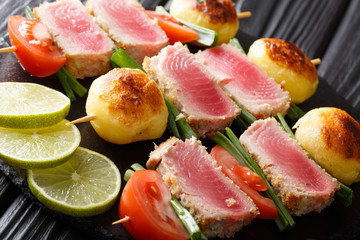 Delicious kebabs on skewers of fresh tuna, tomatoes, potatoes and green onions close-up on the table. horizontal
