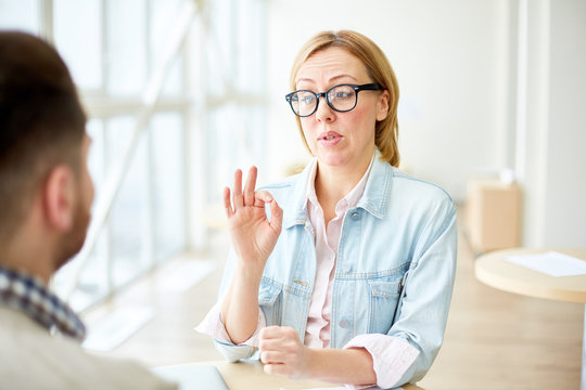 Stylish woman in glasses speaking to man at table in light office room. 