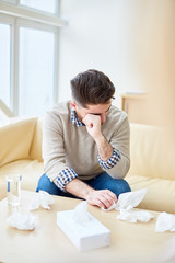 Young man with paper tissues on table crying and suffering from fear while having visit to psychiatrist