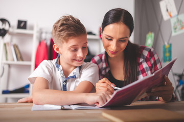 Mother helping her son with homework in teenage room at home