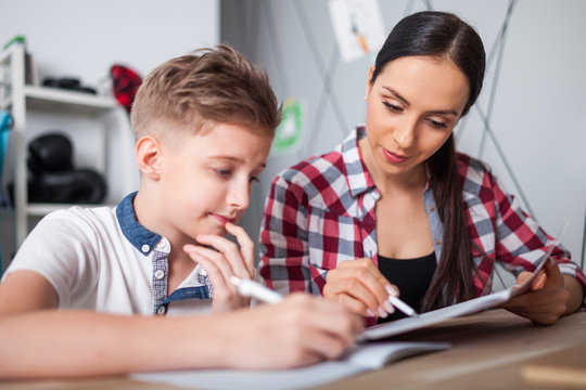 Mother helping her son with homework in teenage room at home