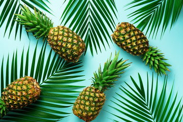 Pineapples and tropical palm leaves on pastel turquoise background. Summer concept. Creative flat...