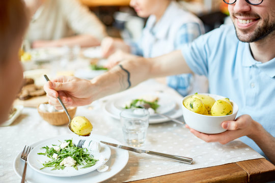 Crop view of smiling male spending time with friends in restaurant and putting potato to plate