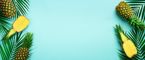 Pineapples and tropical palm leaves on punchy pastel turquoise background. Summer concept. Creative flat lay with copy space. Top view. Banner