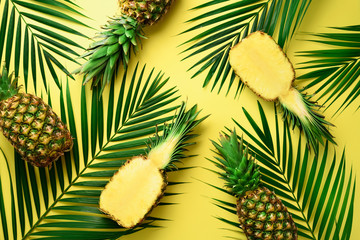 Pineapples and tropical palm leaves on pastel yellow background. Summer concept. Creative flat alay...