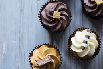 Cupcakes decorated with chocolate,caramel and vanilla icing on a wooden background