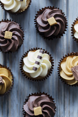 Cupcakes decorated with chocolate,caramel and vanilla icing on a wooden background