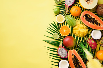 Exotic fruits and tropical palm leaves on pastel yellow background - papaya, mango, pineapple,...