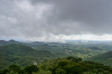 Obraz na płótnie Canvas Mallorca, Rainy dark clouds over green mountainous nature landscape from above