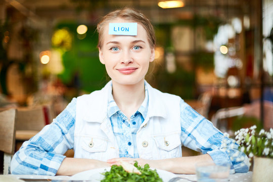 Charming blue eyes woman with scraps paper lion on foreheads smiling and looking at camera on background of blurred cafe