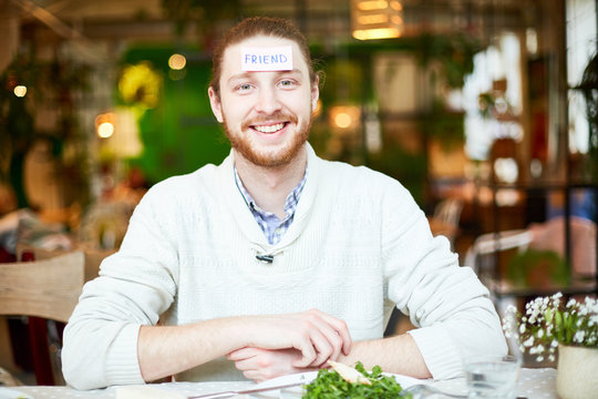 Handsome smiling man with scraps paper friend on foreheads looking at camera on blurred restaurant background