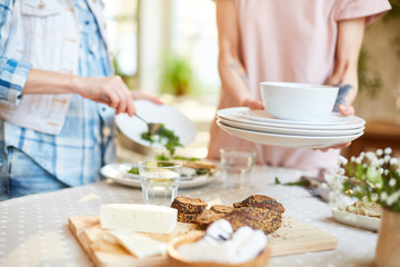 Crop blur view of faceless women removing dishes from table after friends
