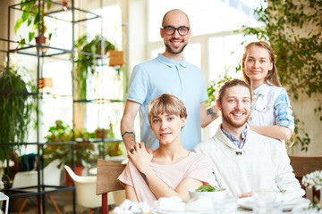 Cheerful company of friends meeting in cafe and looking at camera