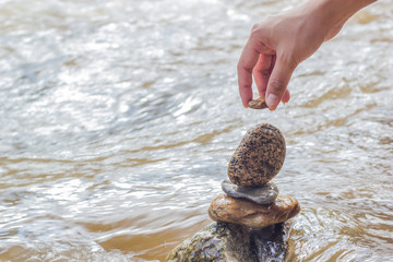 Hand putting stone on stacking stones  on the riverside. The stones are stacked on the river side.