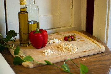 Rice, feta cheese, olive oil, red pepper, and olives on a wood cutting board. Ingredients for an Italian dish