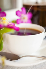 Cup of black coffee and pink blooming flowers  