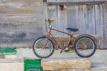Fototapeta na wymiar Old rusty children's bicycle near the wooden wall of an old house