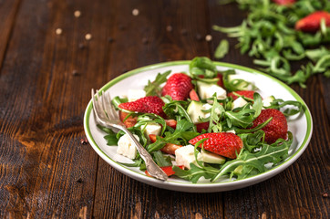 Fresh vegetable strawberry salad on white plate on natural rustic desk.