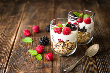 White yogurt with muesli and raspberries in glass bowls on rustic wooden background.