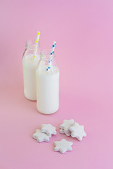 Two bottles of milk and cookies shaped stars on pink background