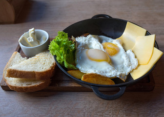 Breakfast, eggs, cheese, potatoes, butter, bread and salad in a frying pan on a wooden tray.