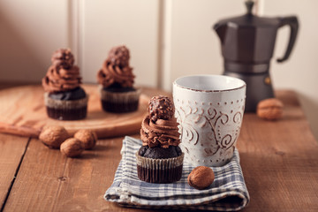 Tasty chocolate cupcakes on wooden board. Cup of coffee. Geyser coffee maker. Violet flowers