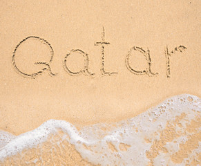 The word Qatar written in the sand on beach