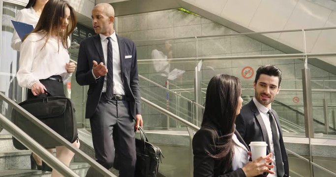 A group of business people, from different ethnic groups, climb the escalators to enter the offices inside the skyscraper. Concept of: team work, internationality and success.