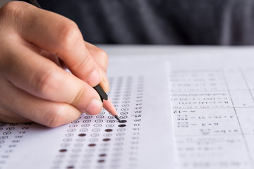 Students hand holding pencil writing selected choice on answer sheets and Mathematics question...