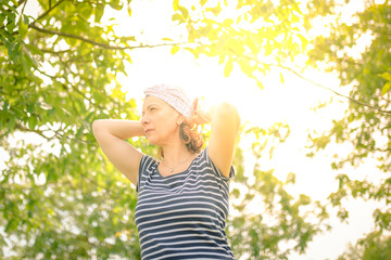 Woman wearing a stylish head scarf in the park Caucasian female outdoor adjust the band in the hair with sunlight in background filter through the branches of trees Portrait of a girl in vintage look