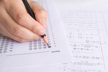 Students hand holding pencil writing selected choice on answer sheets and Mathematics question sheets. students testing doing examination. school exam