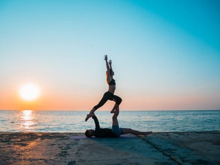 Fit young couple doing acro-yoga at sea beach. Man lying on concrete plates and balancing woman on...