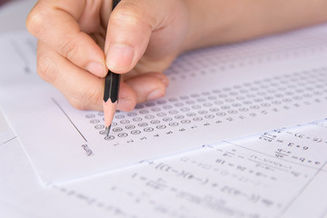 Students hand holding pencil writing selected choice on answer sheets and Mathematics question sheets. students testing doing examination. school exam