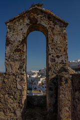 Ancient stone arch of the medieval era. View of a small white Spanish village.