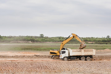 Yellow excavator machine loading soil into a dump truck at construction site