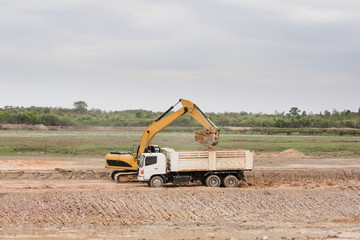 Fototapeta na wymiar Yellow excavator machine loading soil into a dump truck at construction site